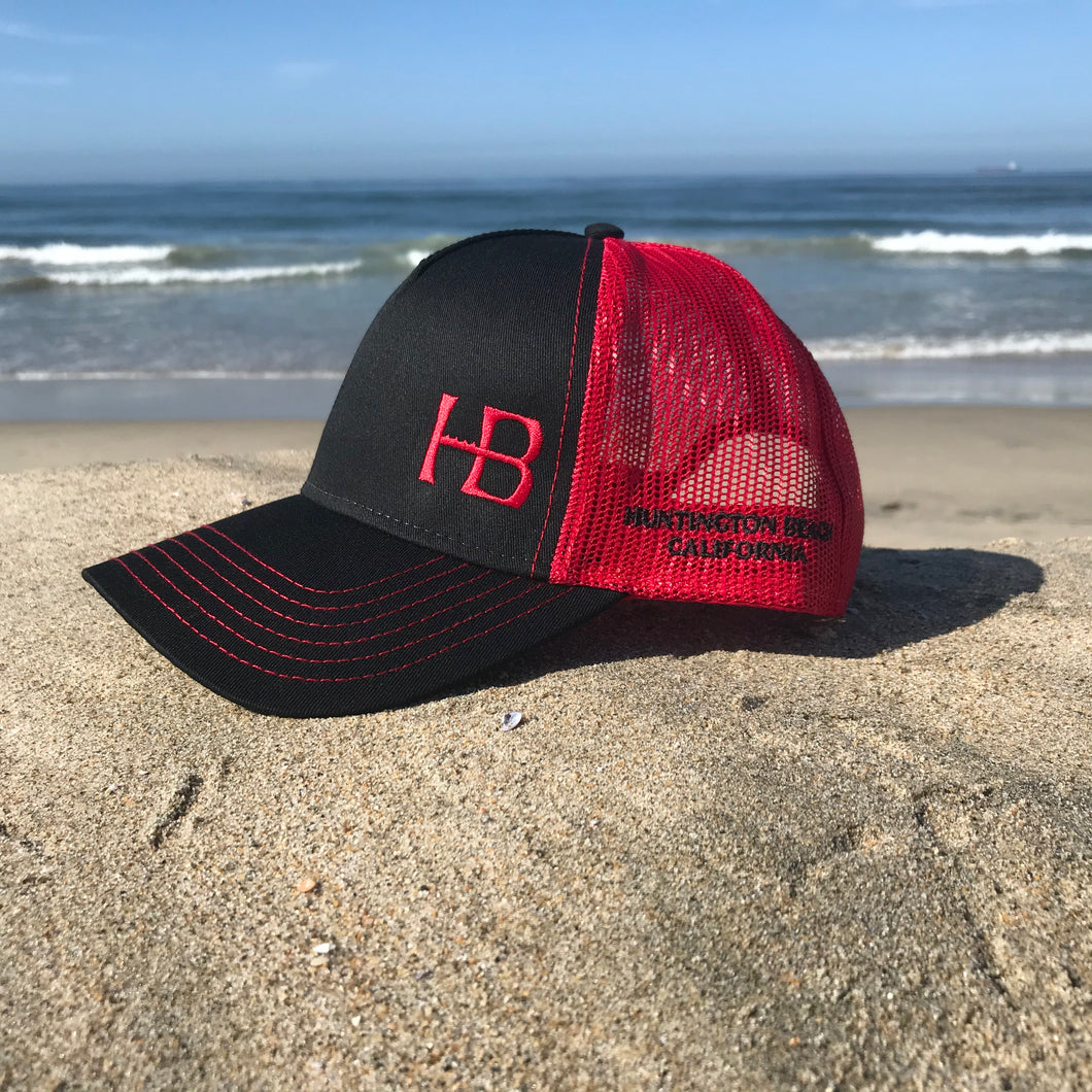 Red embroidered HB in the lower left corner of the front part of this low profile, snapback trucker hat. Huntington Beach California is embroidered on the left side of the hat in black stitching.  5 panel, Low profile, structured firm front panel, pre-curved visor, red mesh back, cotton blend twill front consisting of 65% Polyester and 35% Cotton.