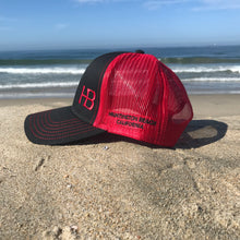 Load image into Gallery viewer, Red embroidered HB in the lower left corner of the front part of this low profile, snapback trucker hat. Huntington Beach California is embroidered on the left side of the hat in black stitching.  5 panel, Low profile, structured firm front panel, pre-curved visor, red mesh back, cotton blend twill front consisting of 65% Polyester and 35% Cotton.
